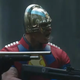 Crop photo of John Cena as Peacemaker, excitedly firing a gun in the woods.